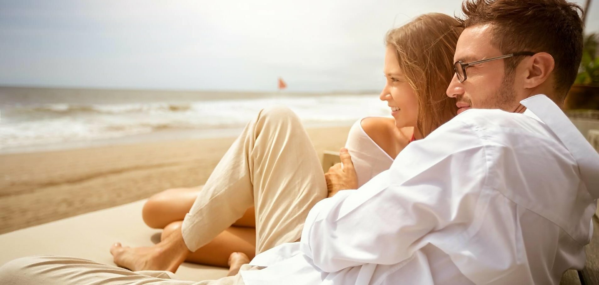 Ung par sidder og krammer på stranden og nyder udsigten