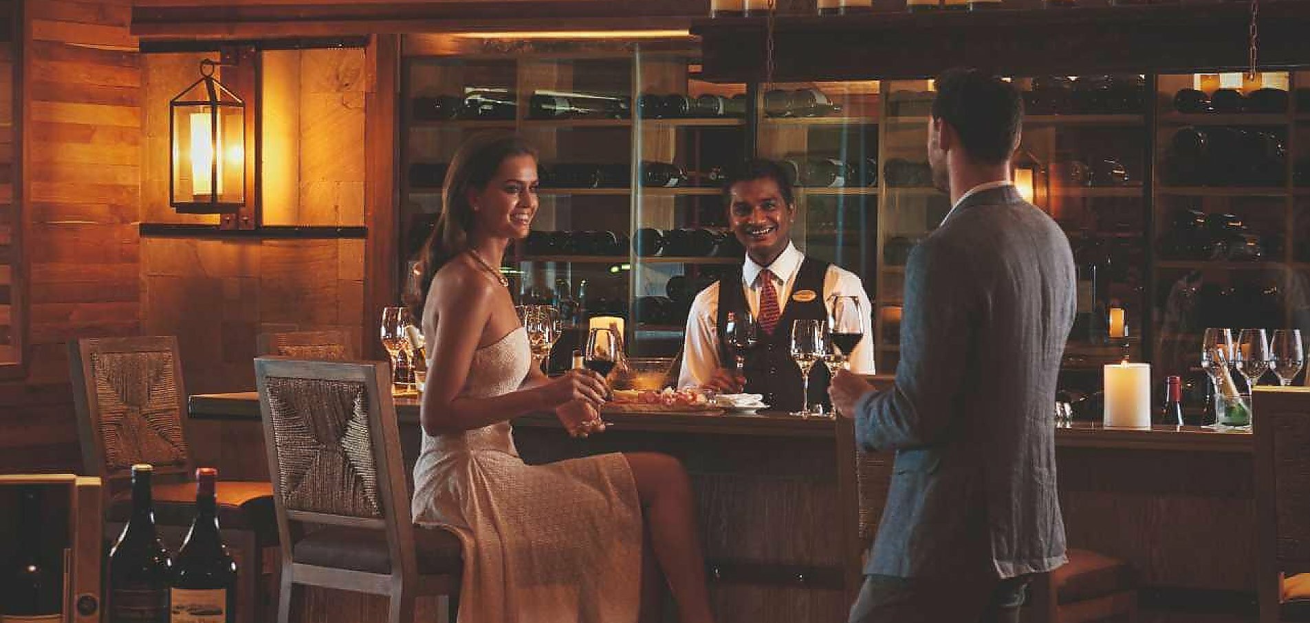 Ung kvinde i flot kjole kigger på ung mand ved baren på Constance Belle Mare Plage resort